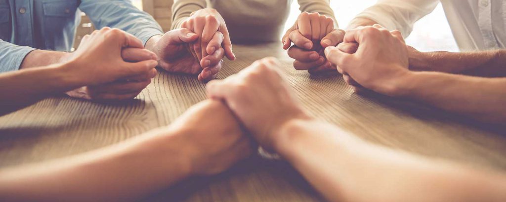 a photo of people sitting at a table holding hands and praying